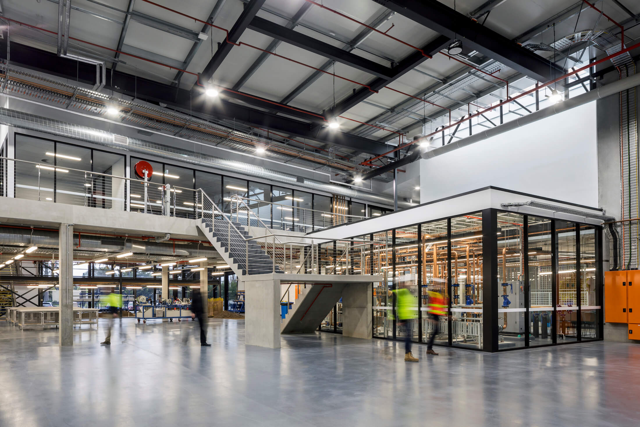 Wide shot of a four storey training factory space with central control room, glass walled with exposed copper pipes.