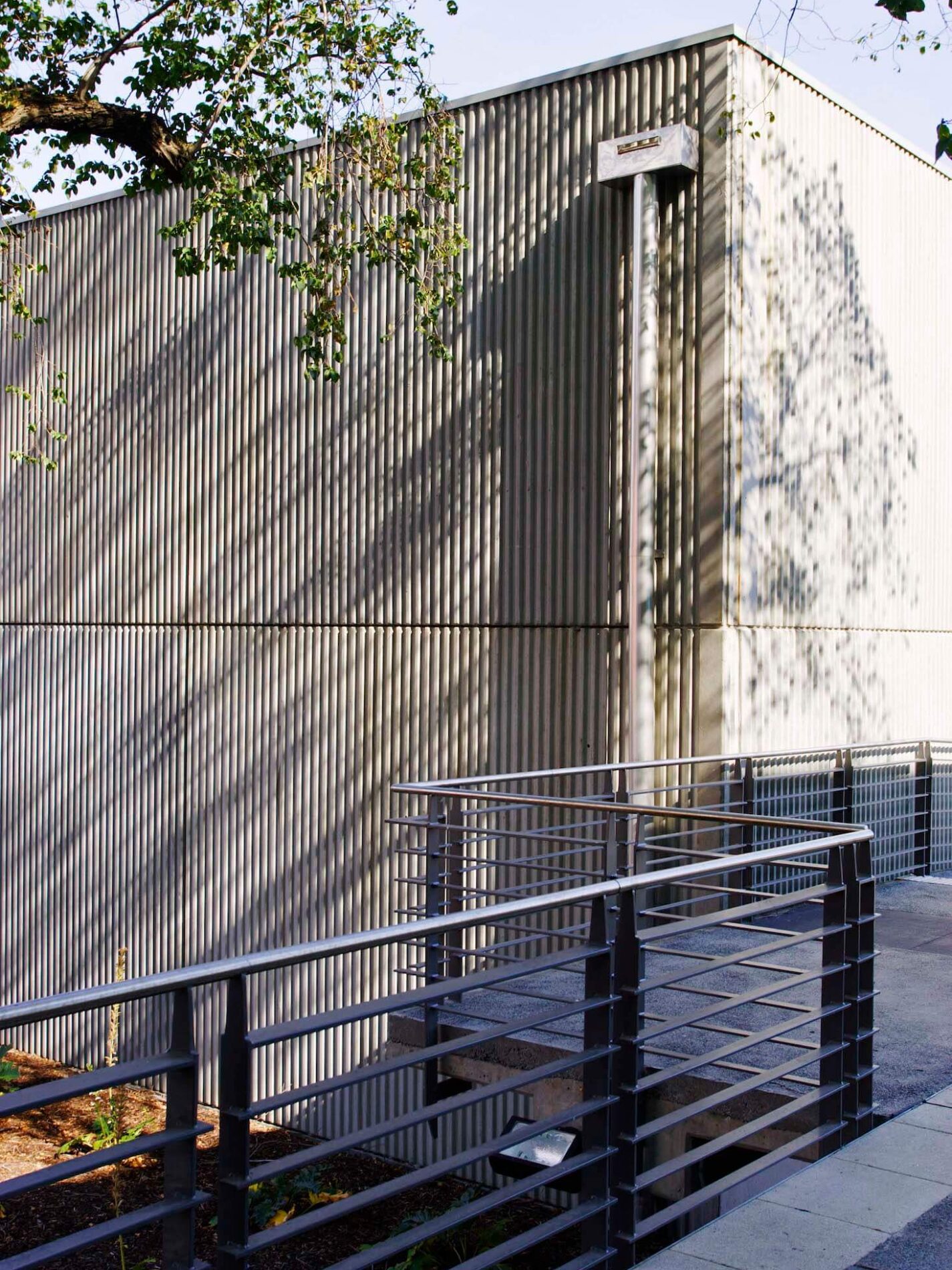 Metal cladding building and timber walkway with balustrade, in dappled shade