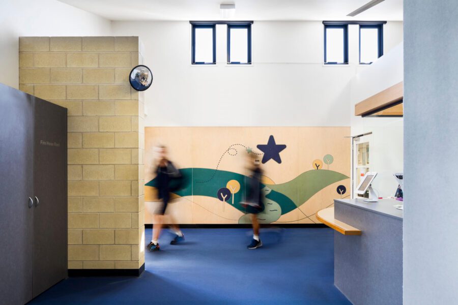 Plywood mural alongside student entry features school emblem graphic artwork with trees, a star and a river