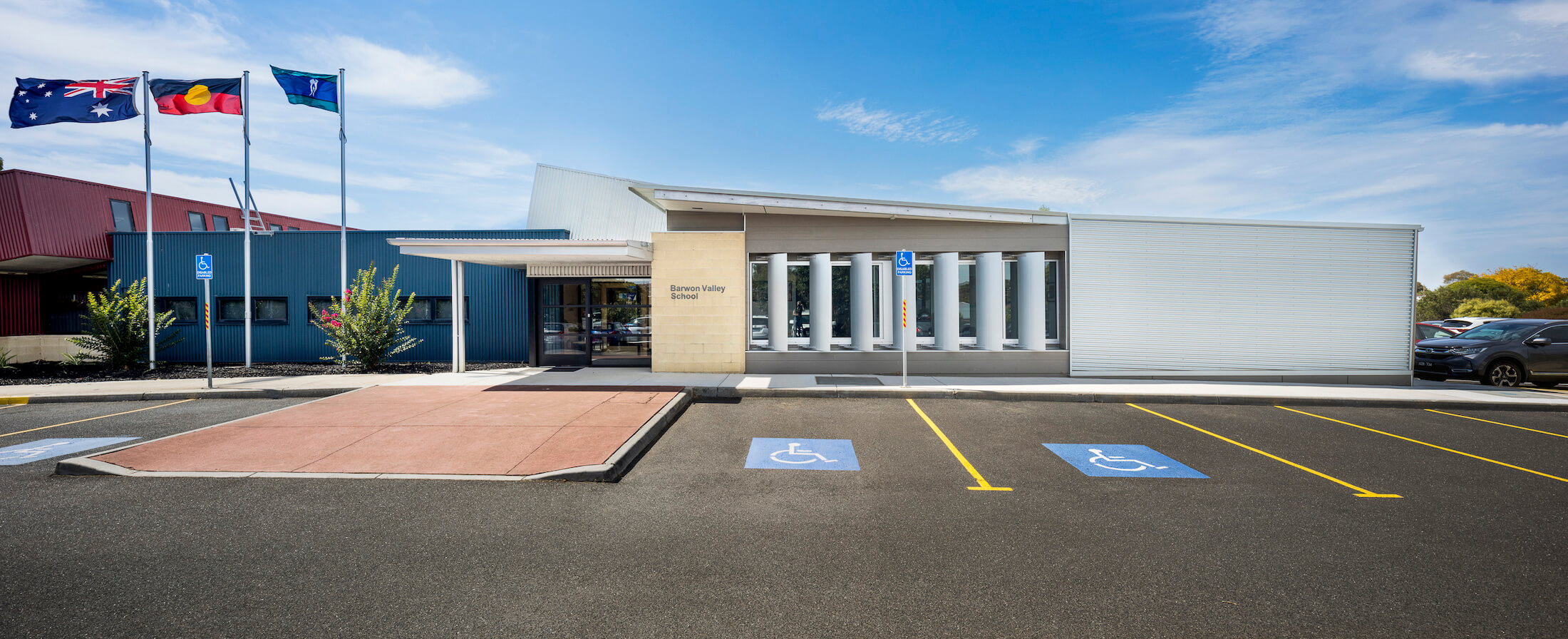 School building facade with Australian, Aboriginal and Torres Strait Islander flags flying, disabled car parking