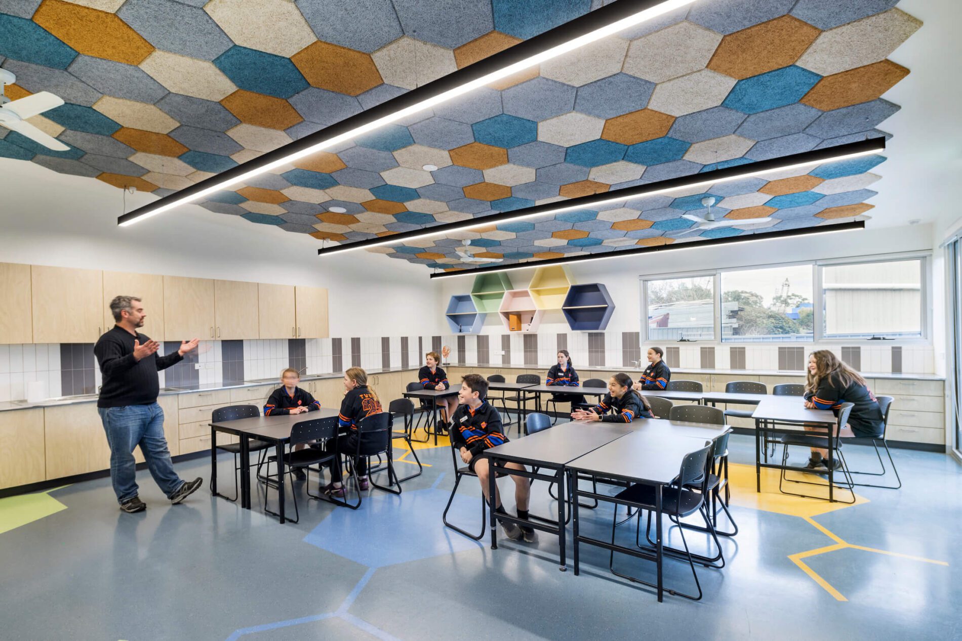 Students smiling, listening to teacher in science laboratory with honeycomb acoustic panel ceiling
