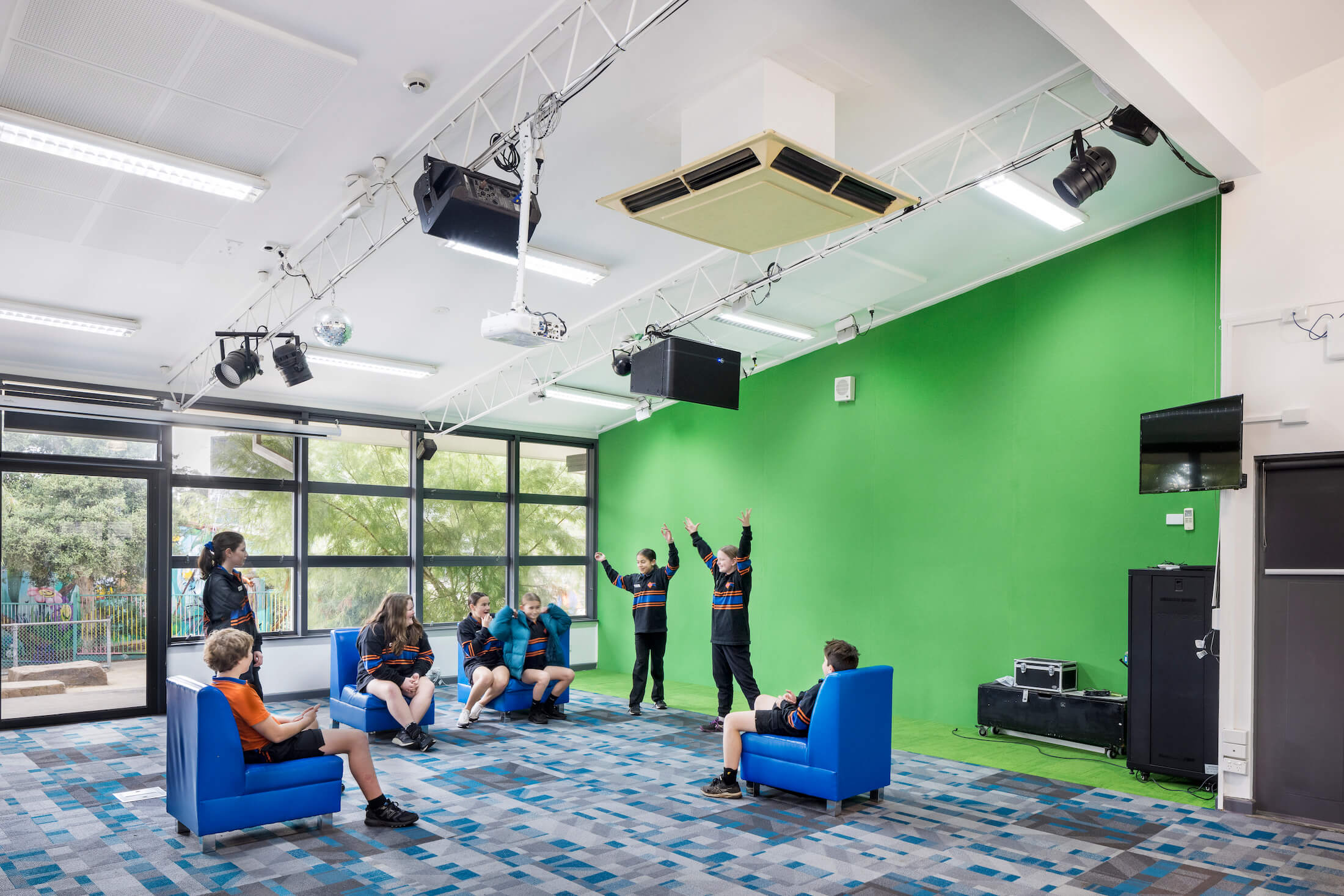 Students perform in front of a green screen wall in a media room
