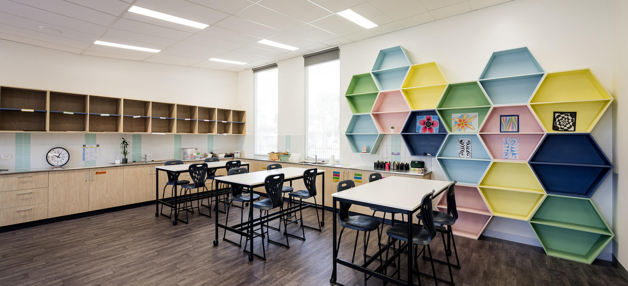 Art room with tables and hexagonal colourful nook wall feature, wet area sink