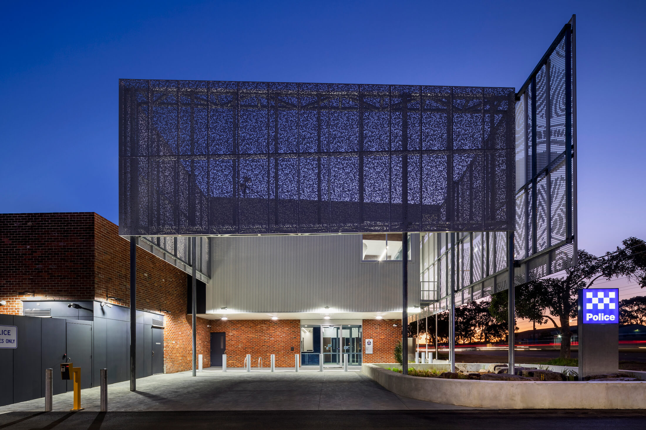 Perforated steel screen facade over police station forecourt at night
