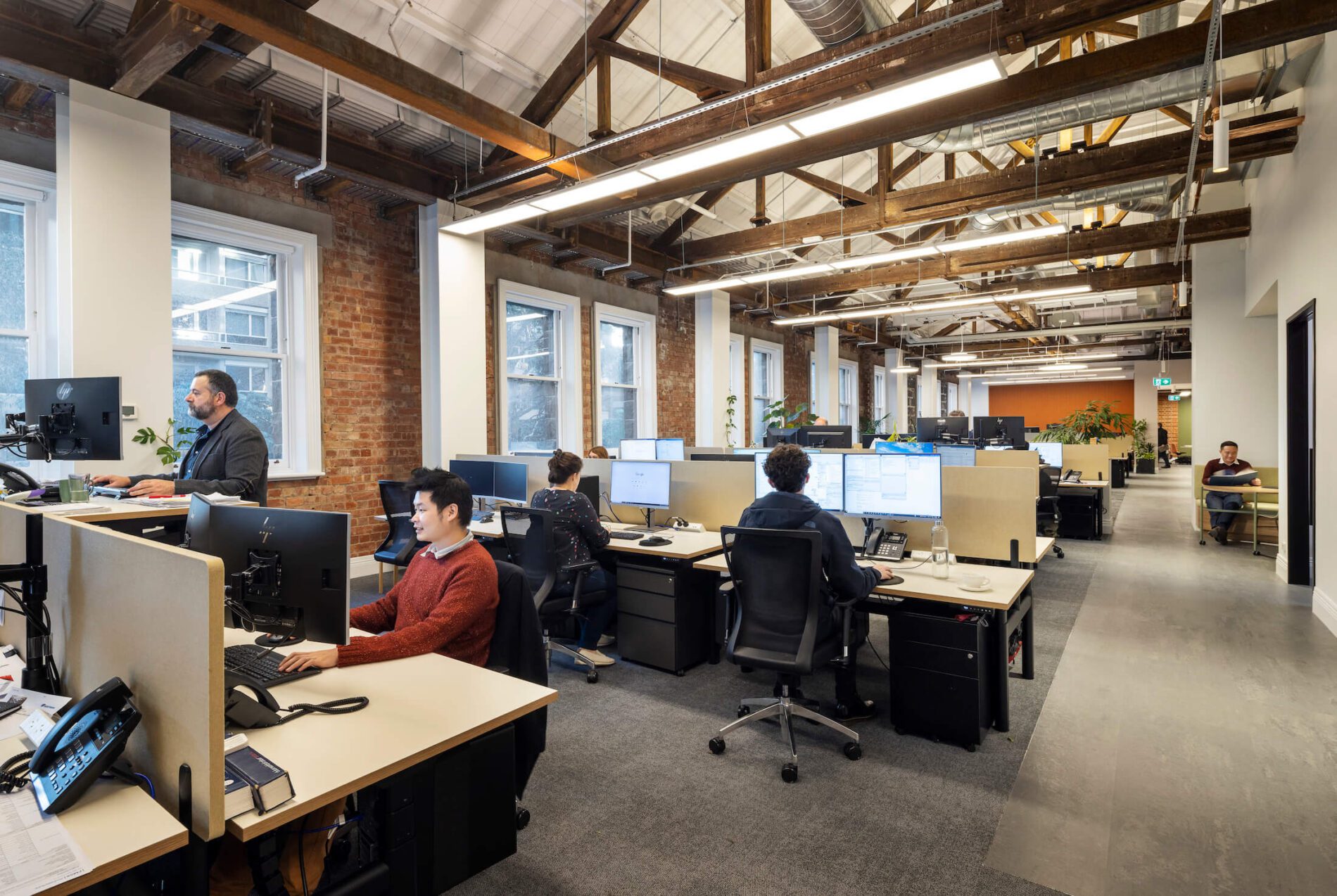 Staff sit and stand at desks within Foreground office, exposed timber beams in warehouse style space.
