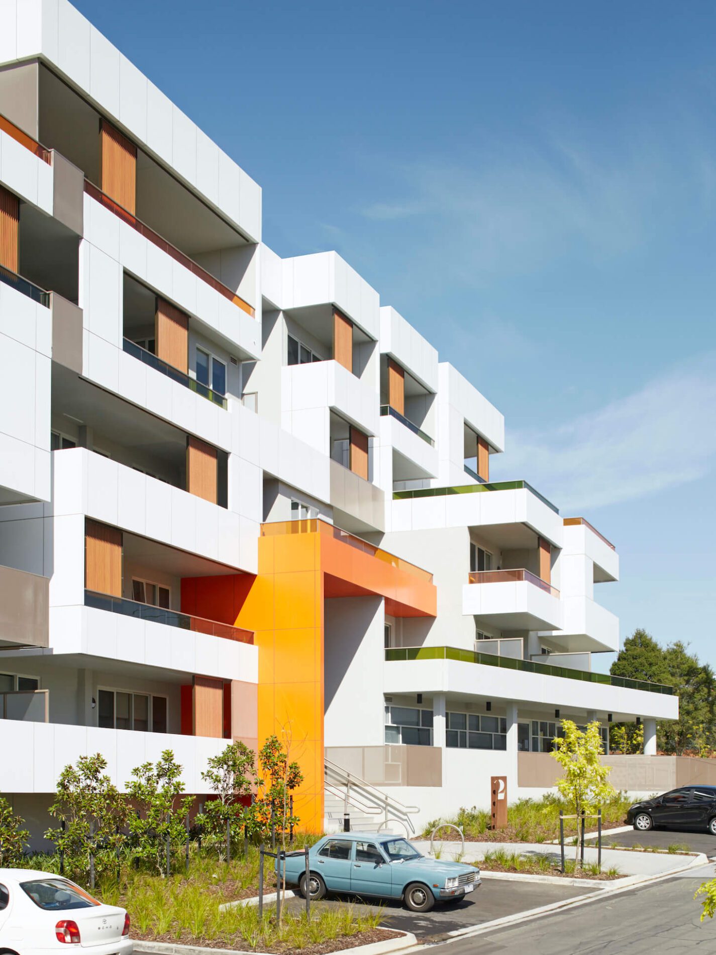 A white multi-storey apartment building with orange and green feature elements, cars parked out front