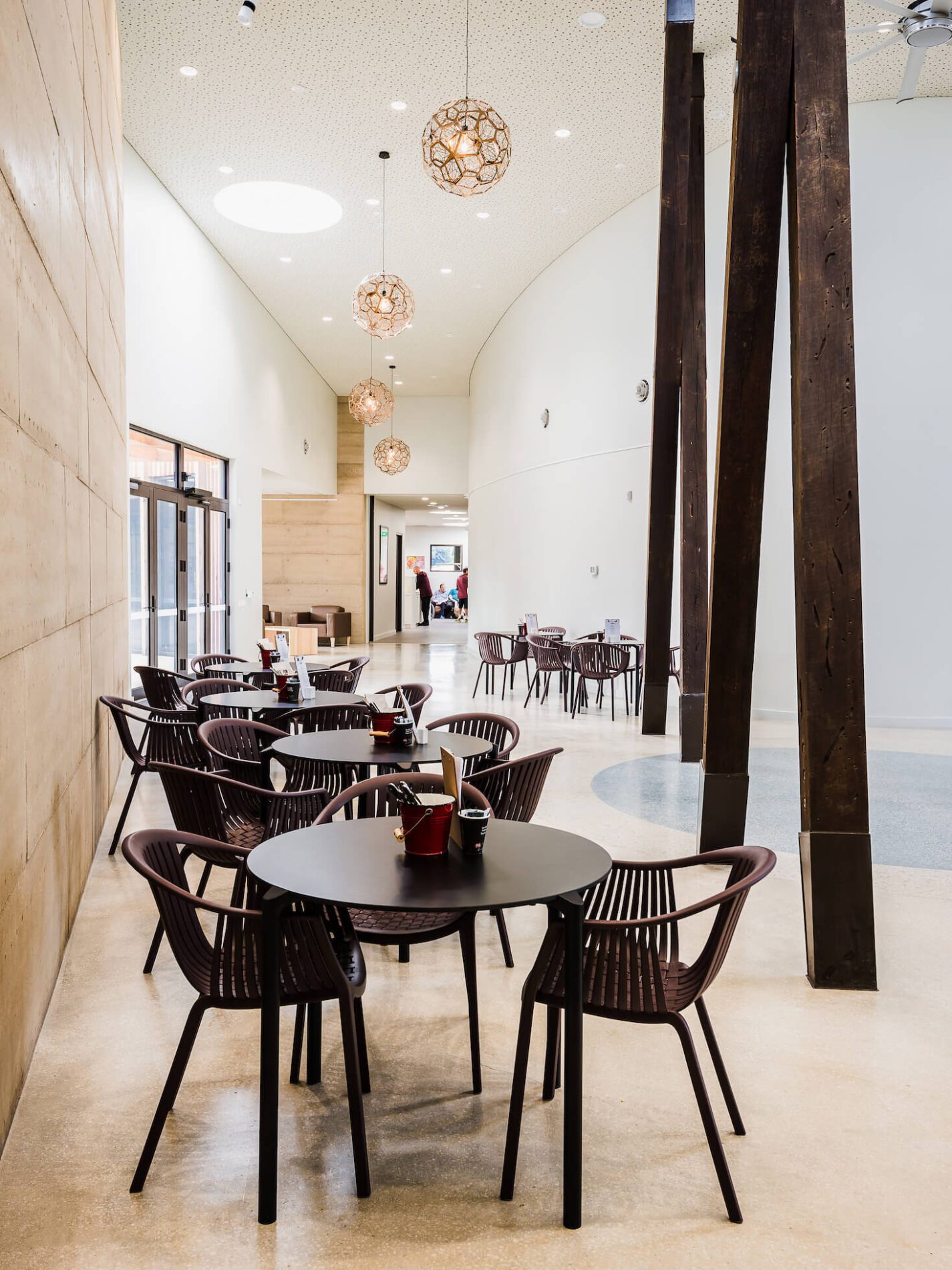 Interior image of café seating in high ceiling atrium space with feature timber structural columns