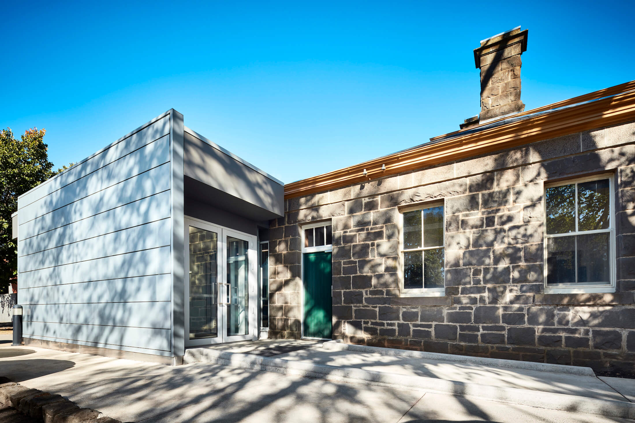 Bluestone heritage building with green door and contemporary addition with public entrance