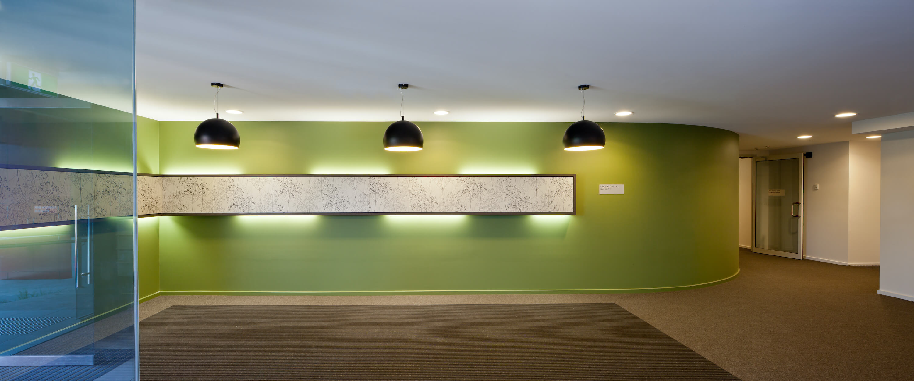 Curved green feature wall in building entry, black pendant lights