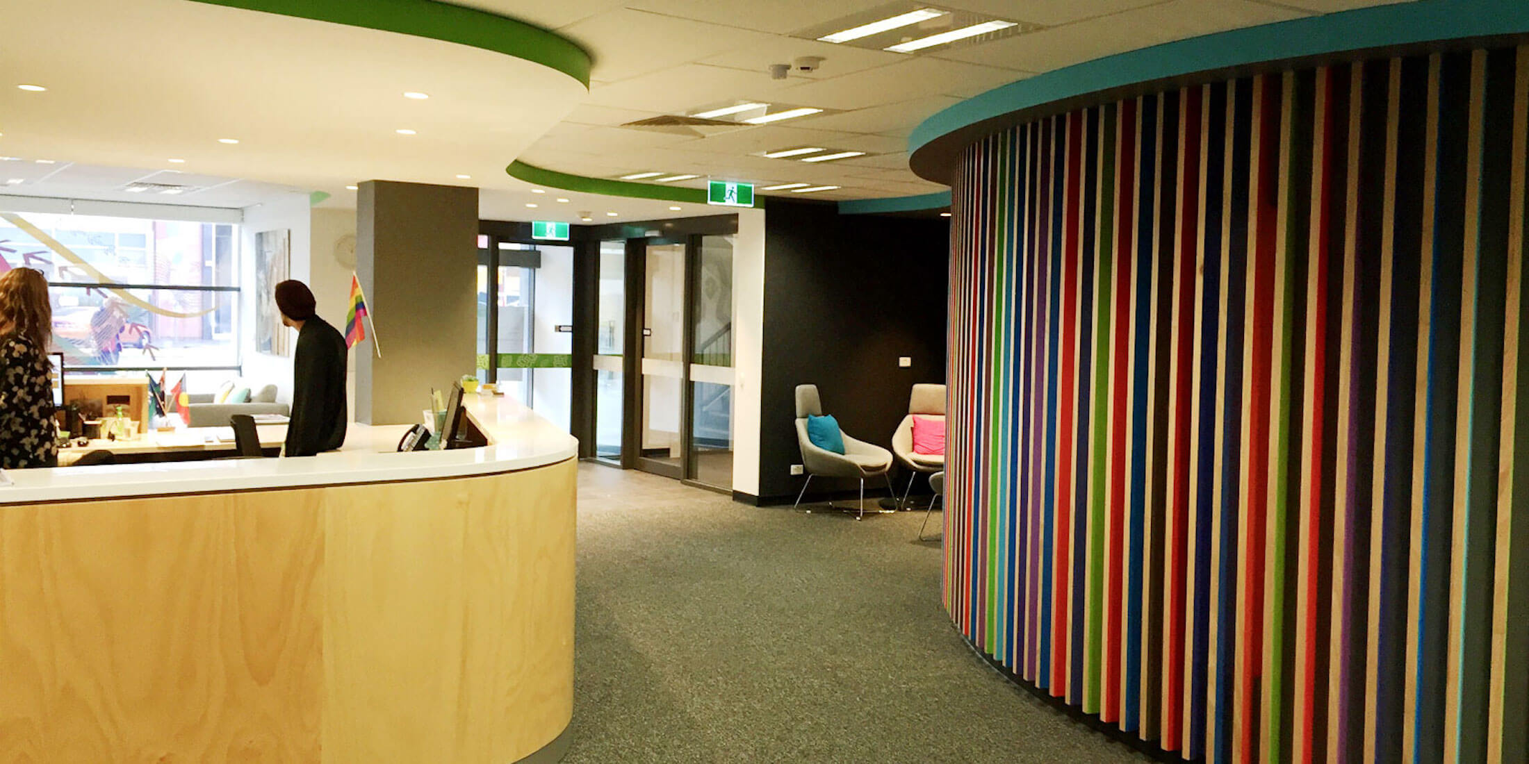 Rainbow coloured ribbed detail on wall screening a waiting area, reception desk to the left