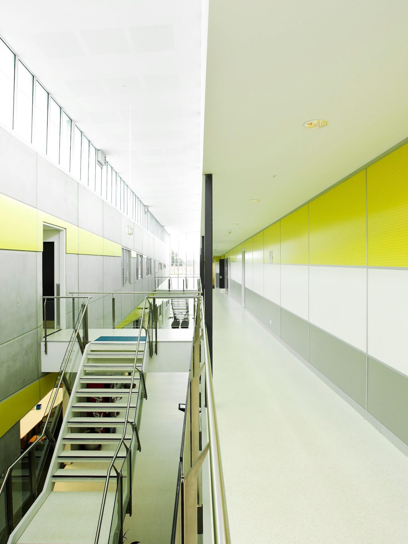 Hallway view within police station, brightly lit from double height void over internal staircase, yellow panelling on walls