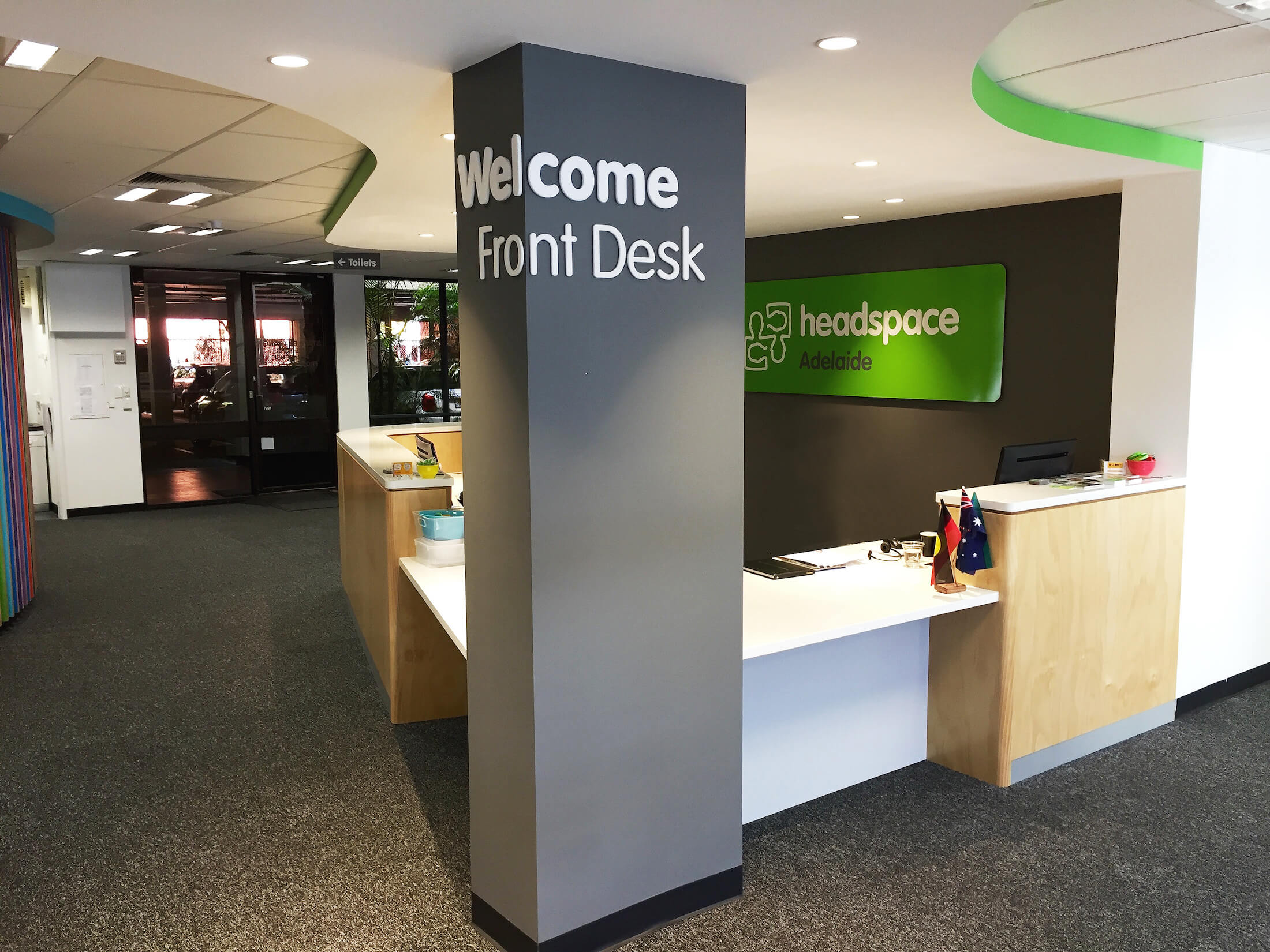 Sign stating "Welcome Front Desk" on grey pillar. Green "headspace Adelaide" sign behind reception