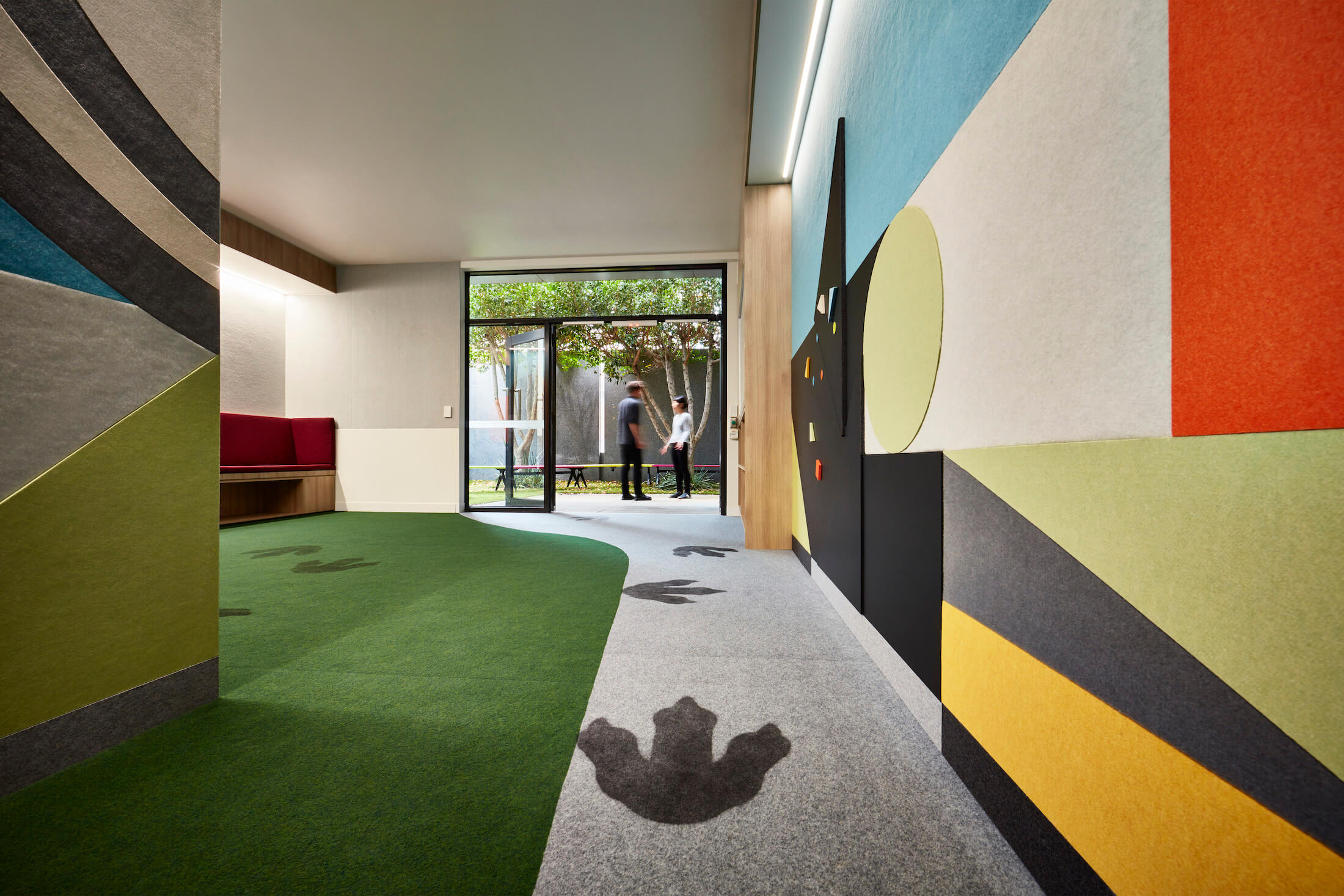 Felt acoustic wall panels in colourful patterns in hallway between court spaces and leafy courtyard