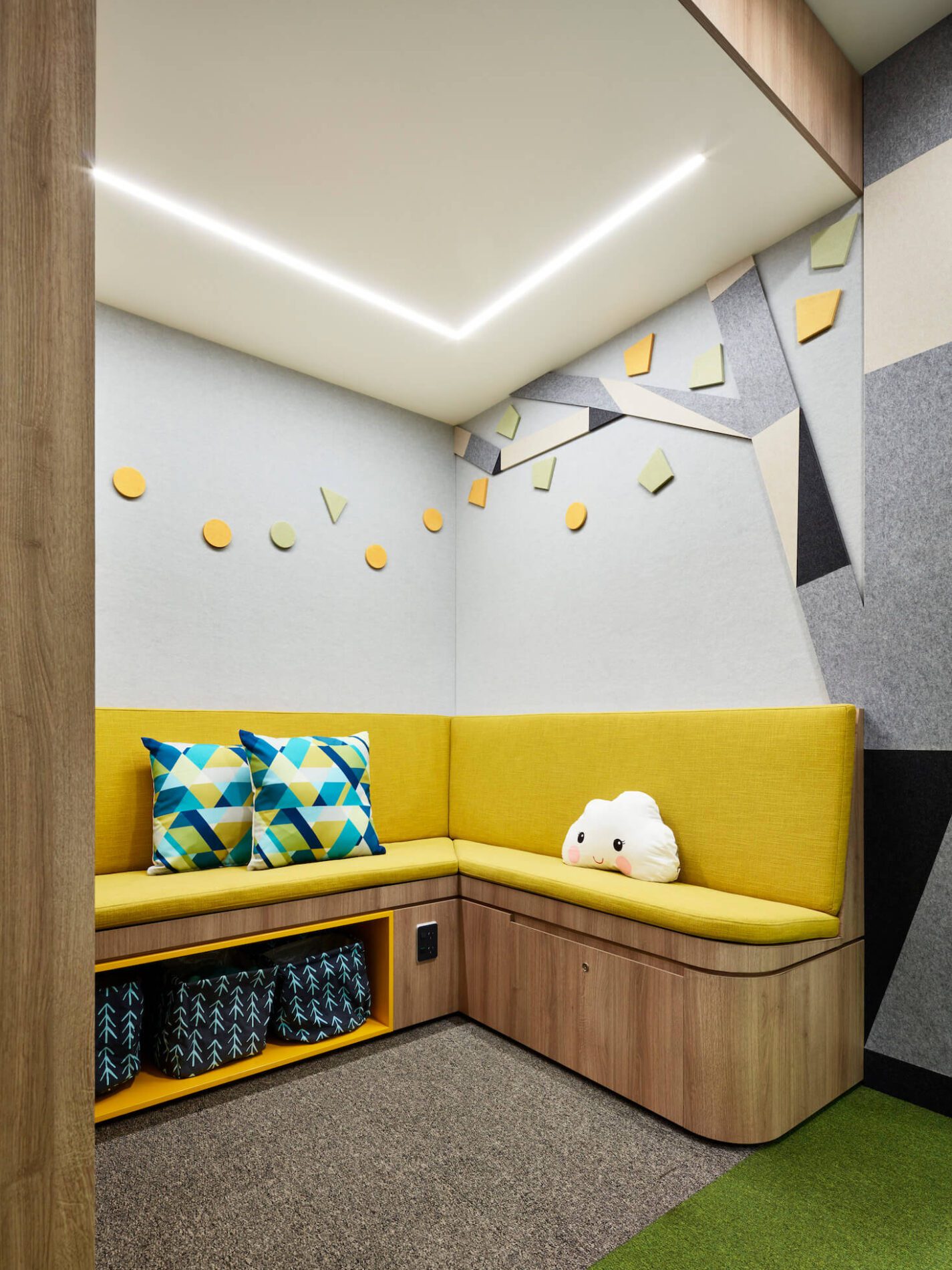 Cubby nook with yellow padded bench seating, felt wall decals, cloud pillow and patterned toy storage bags