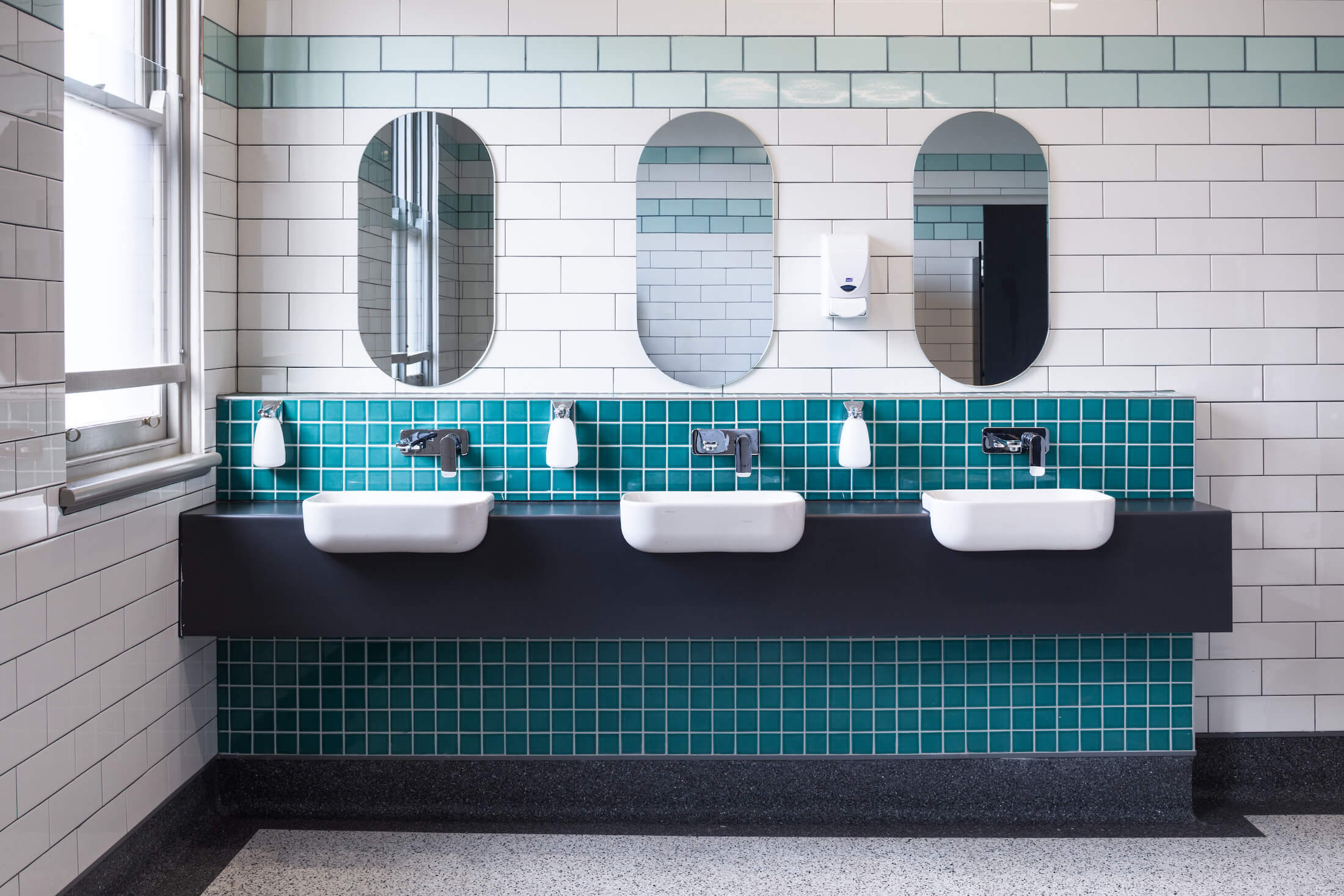 Shared bathroom with three vanities, three oval mirrors and aqua and white tiles