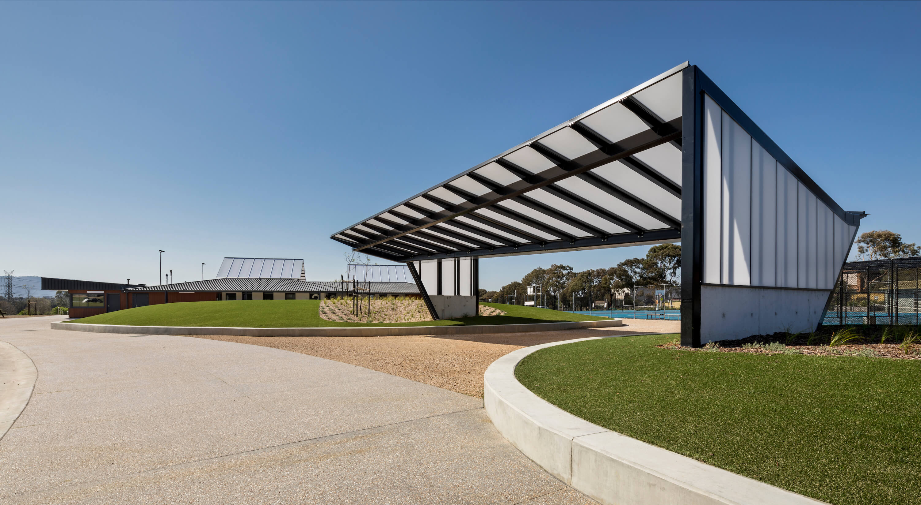 Shade structure straddles two grassy mounds next to tennis court