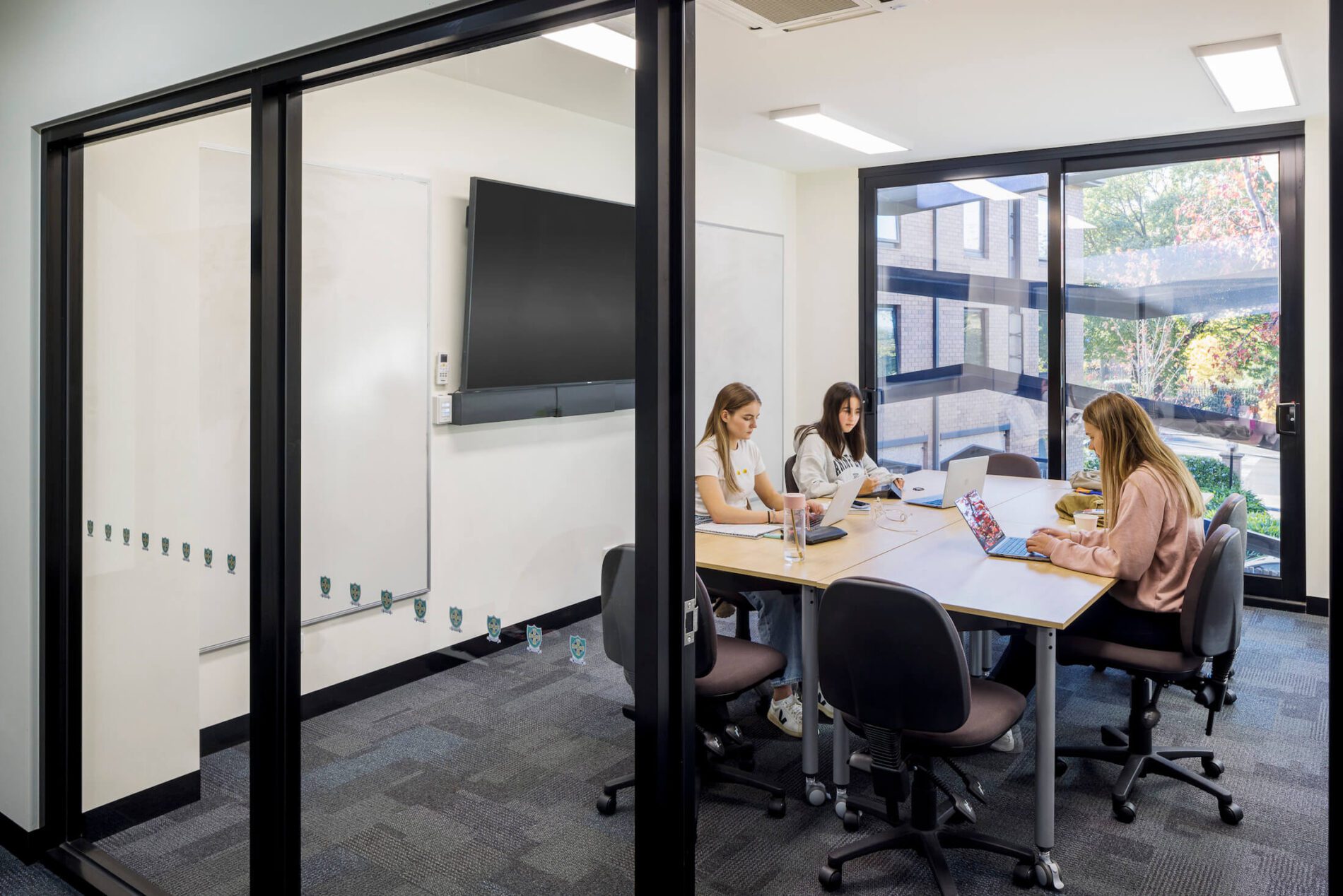 Students sit in meeting room behind windows to internal space, views beyond
