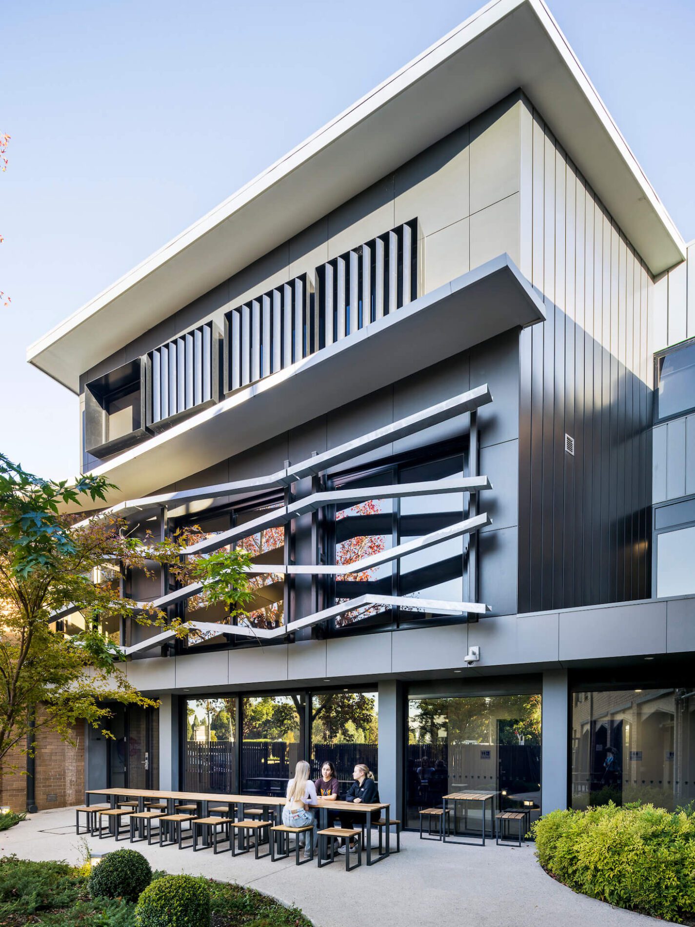 Contemporary building with window barrier feature, landscaping and outdoor dining tables and chairs below