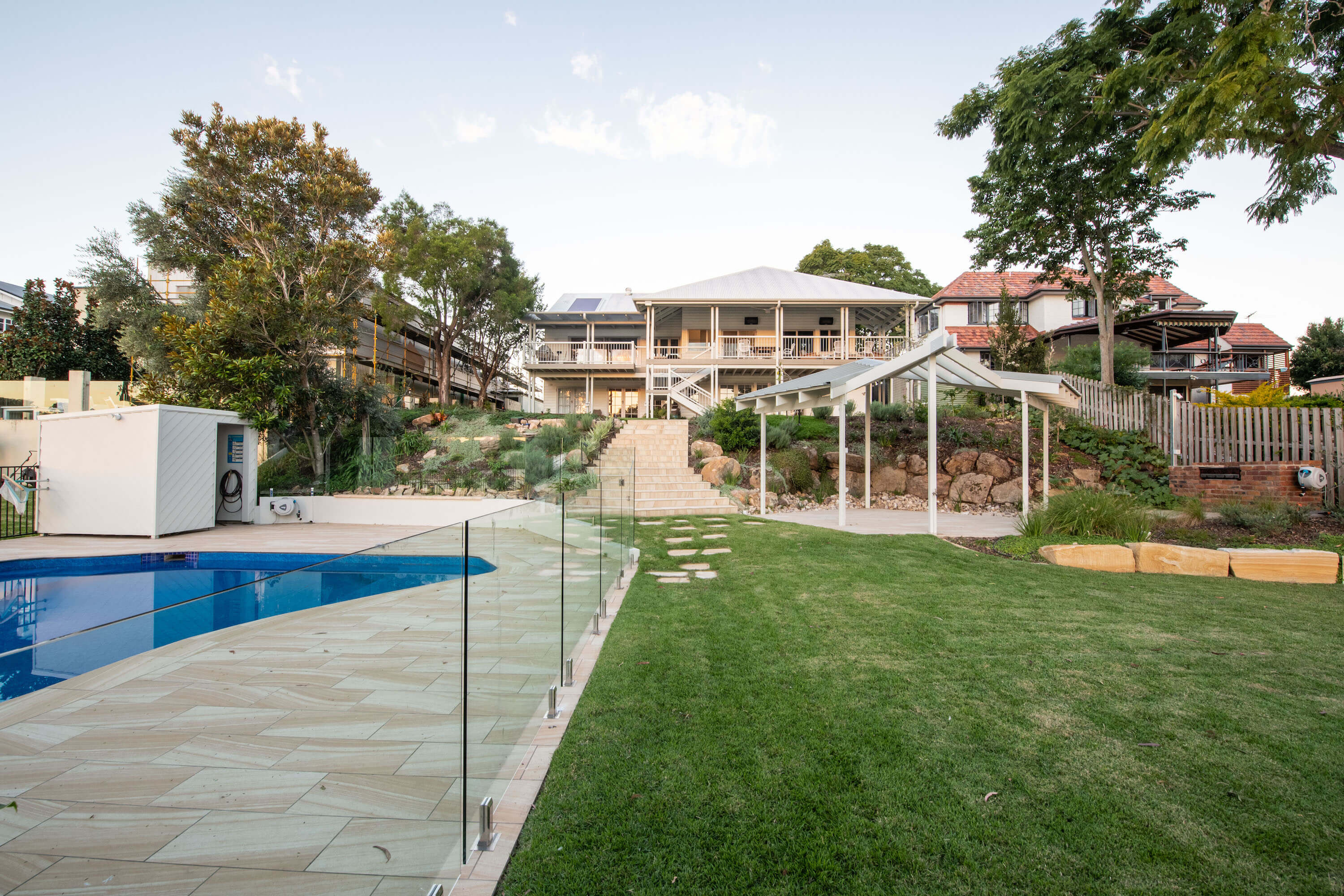 Vast landscaped area with pool and pergola below Queenslander home