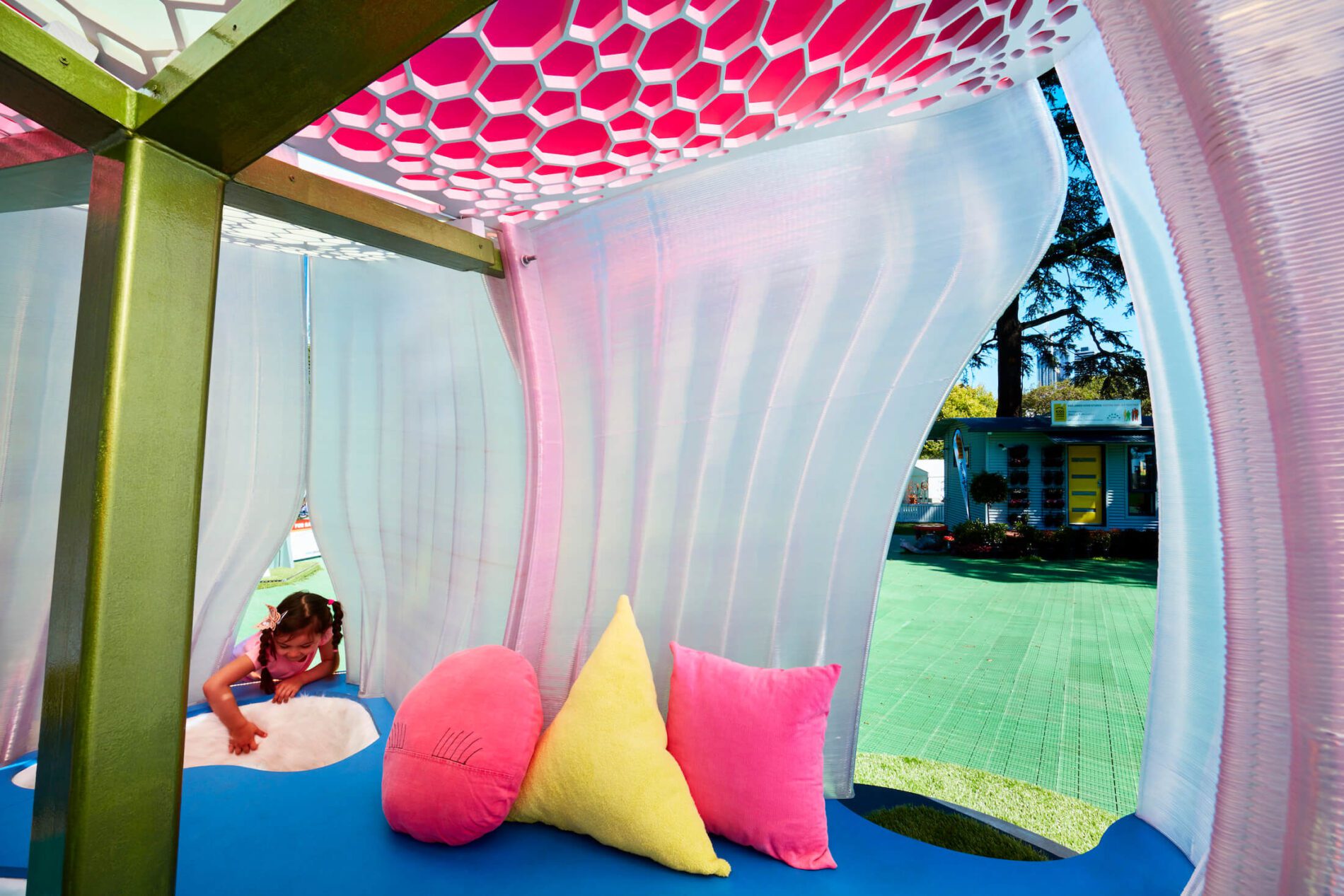 Inside of pink formed structure with soft pink and yellow cushions and playful pink honeycomb ceiling