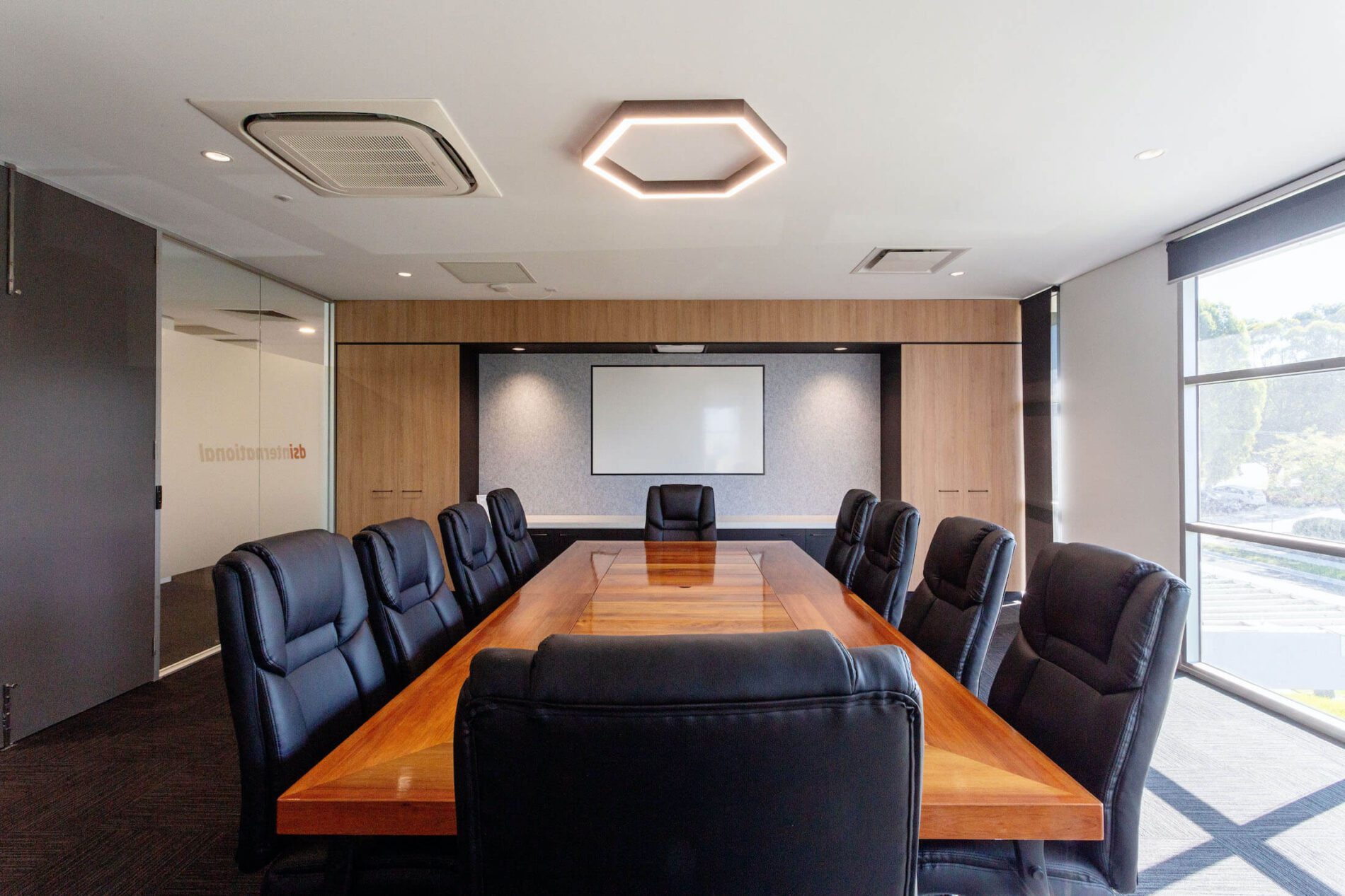 Boardroom with hexagonal light overhead, black chairs, timber table