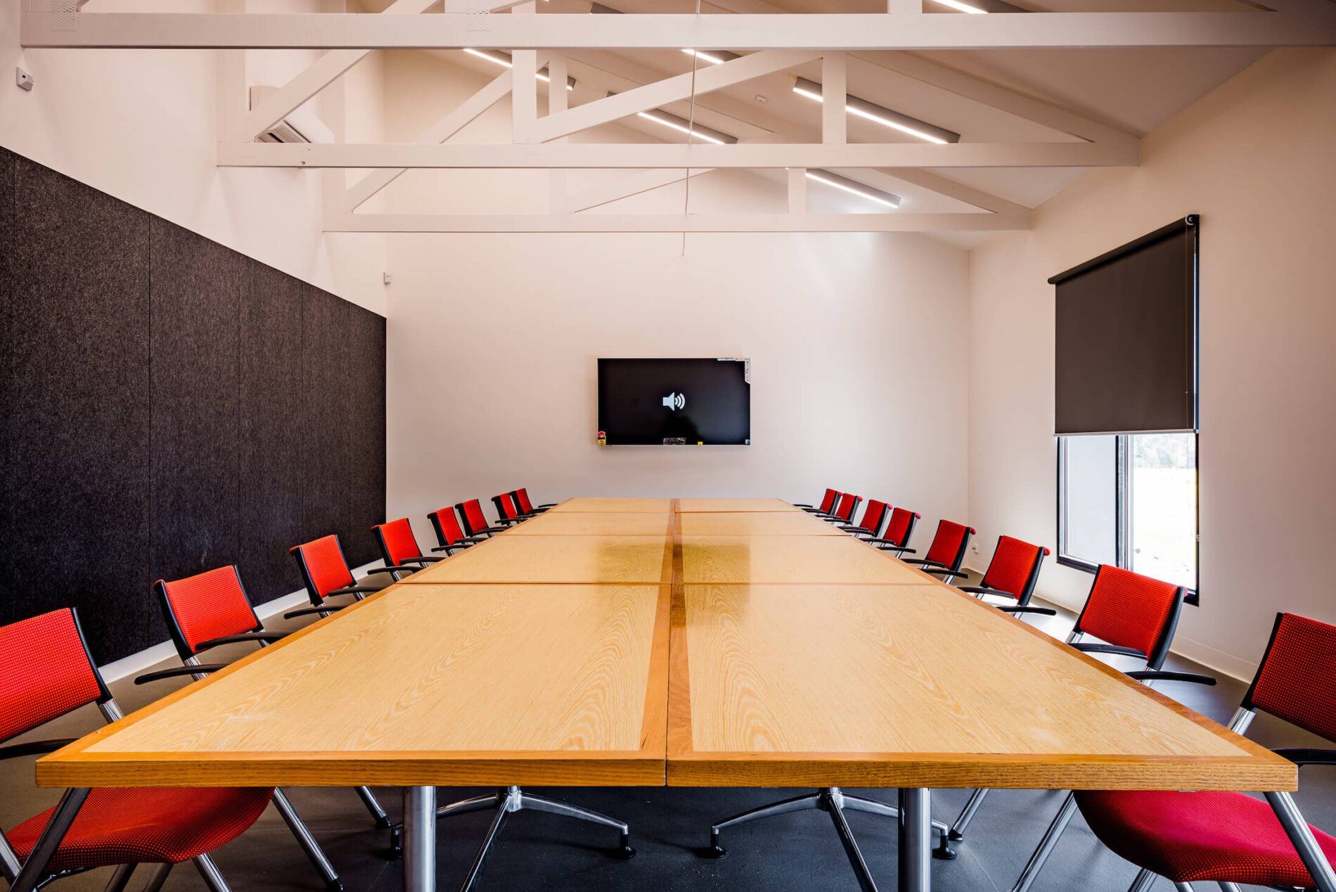Boardroom with dark pinboard wall, 16 red chairs around 8 joined timber tables
