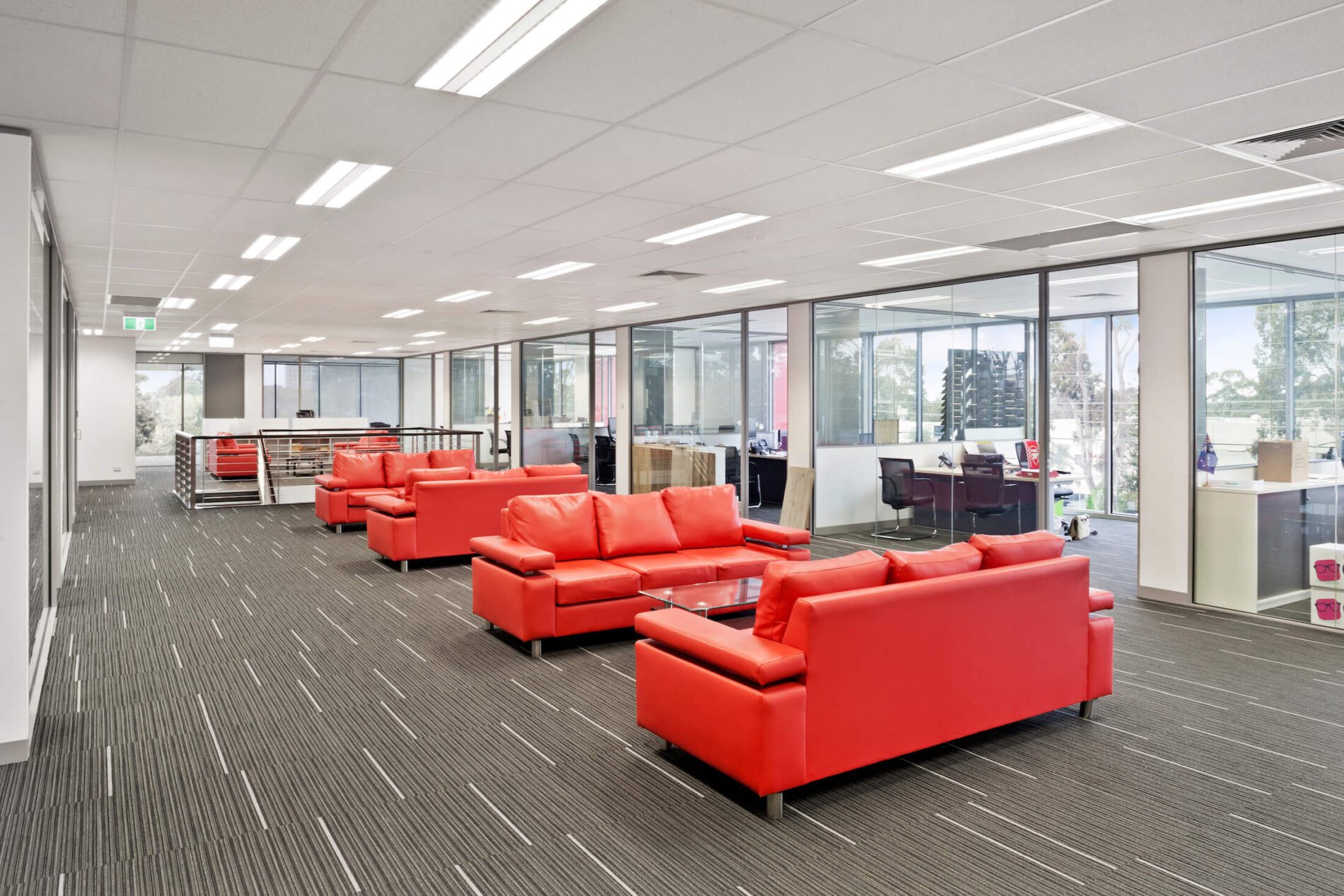 Red leather lounges and coffee tables in breakout space beyond offices in commercial headquarters