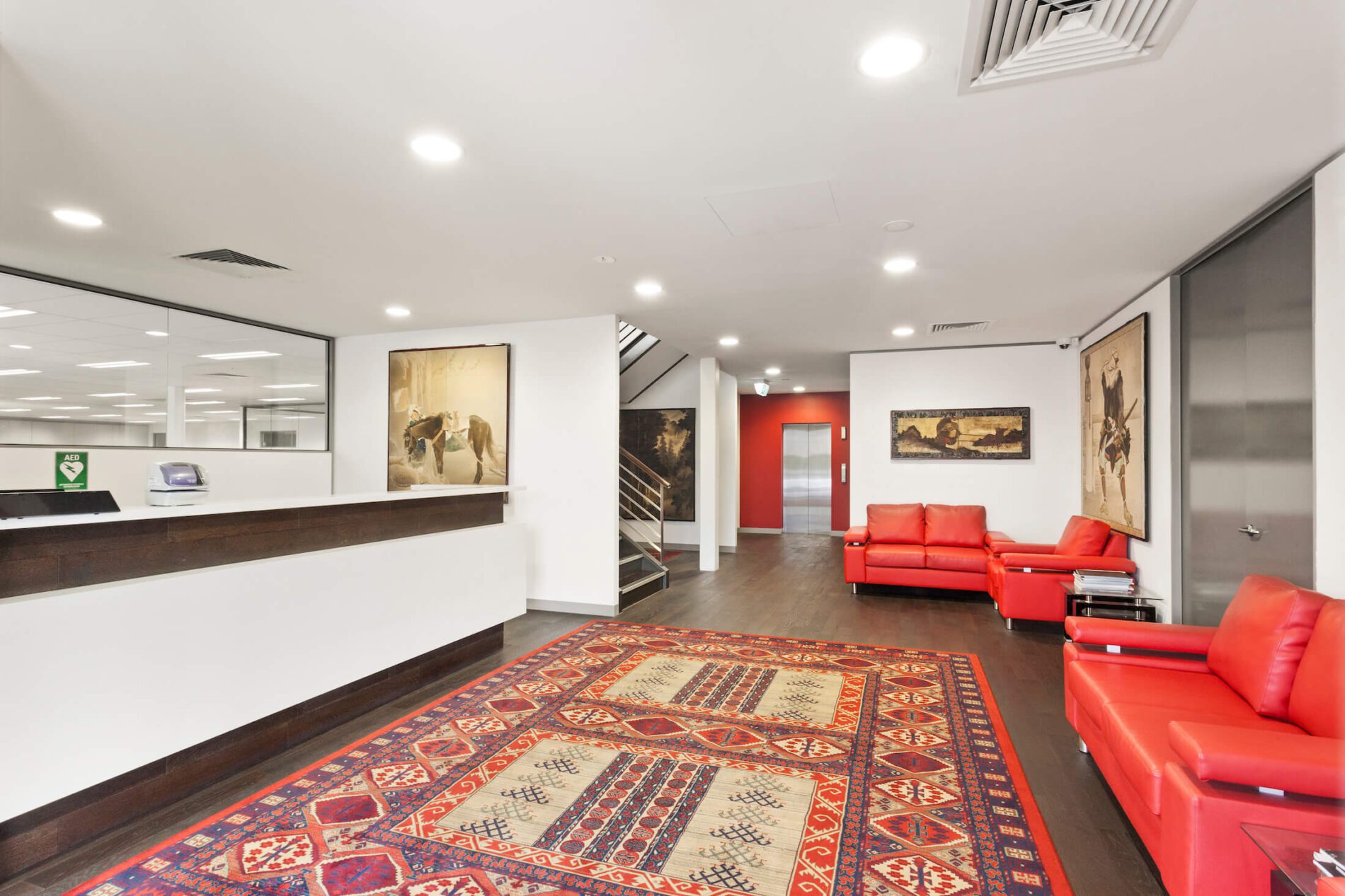Foyer area in reception with red leather couches, rug on floor and artwork on walls