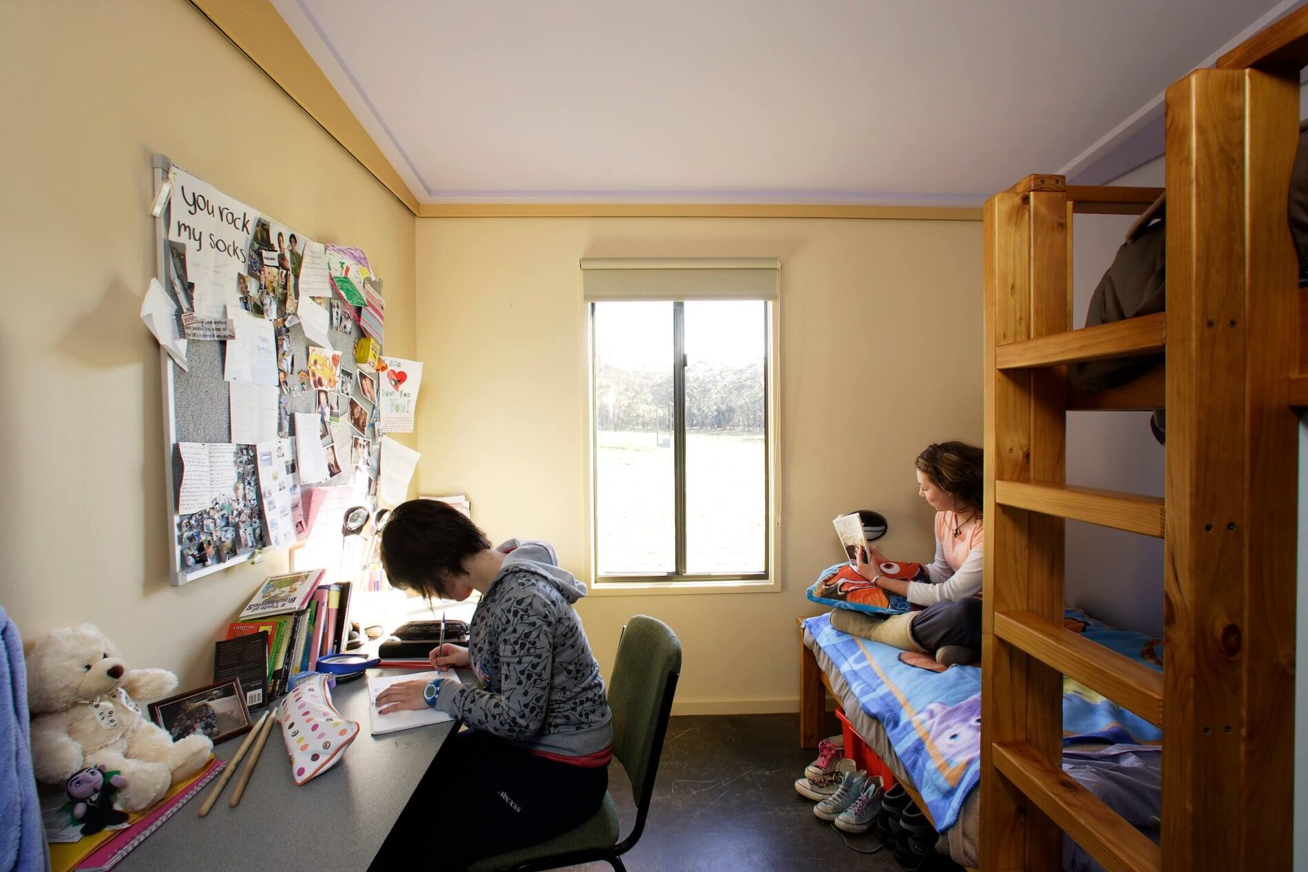 Students sit at desk writing, and on bed, reading in student accommodation