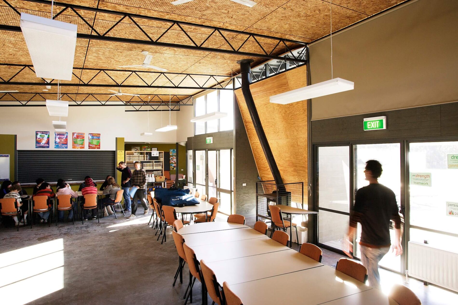 Interior view of large mess hall with exposed horizontal metal trusses and perforated ply ceilings