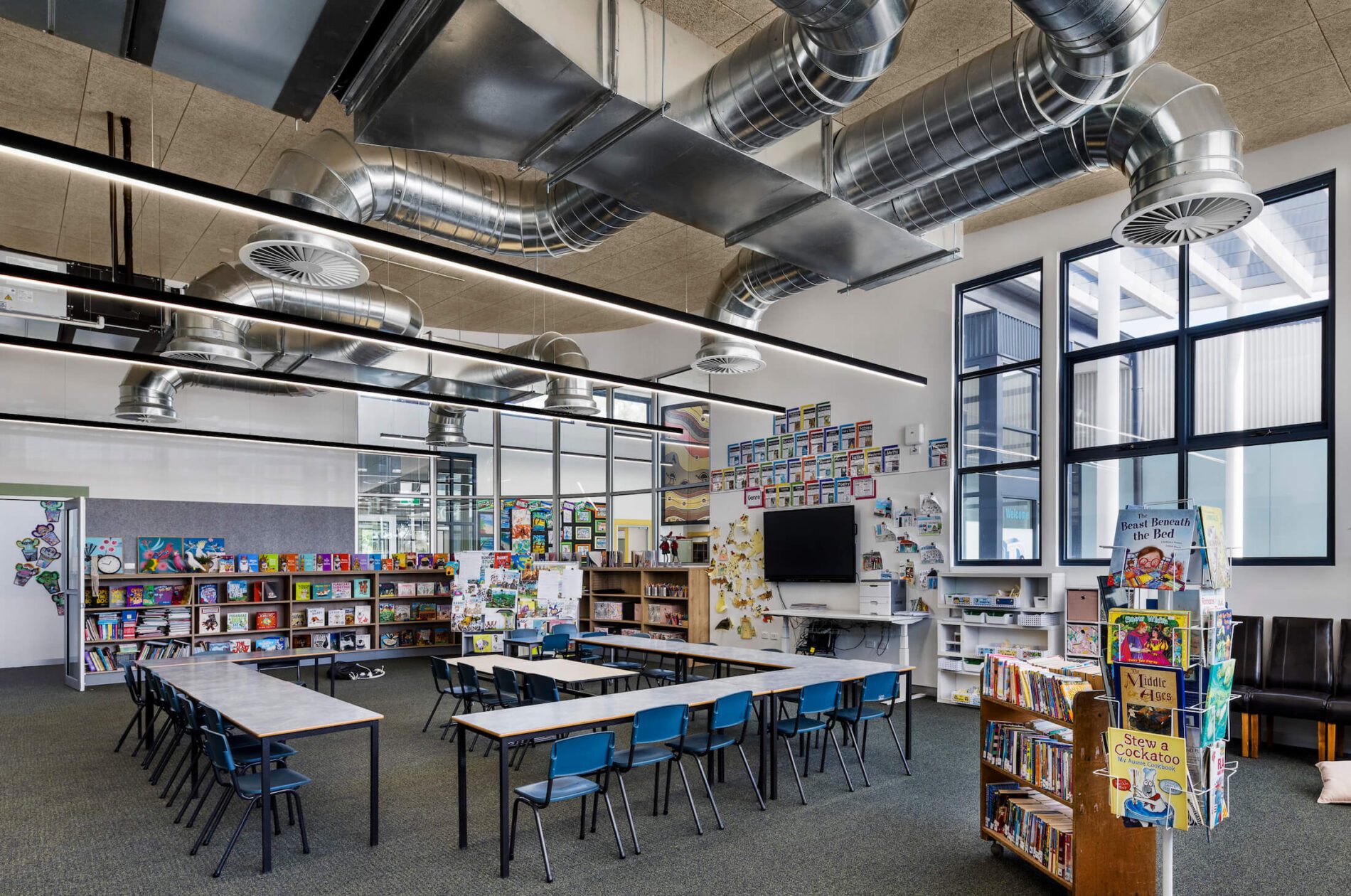 School library with bookshelves and desks arranged in square. Ducted ventilation above.