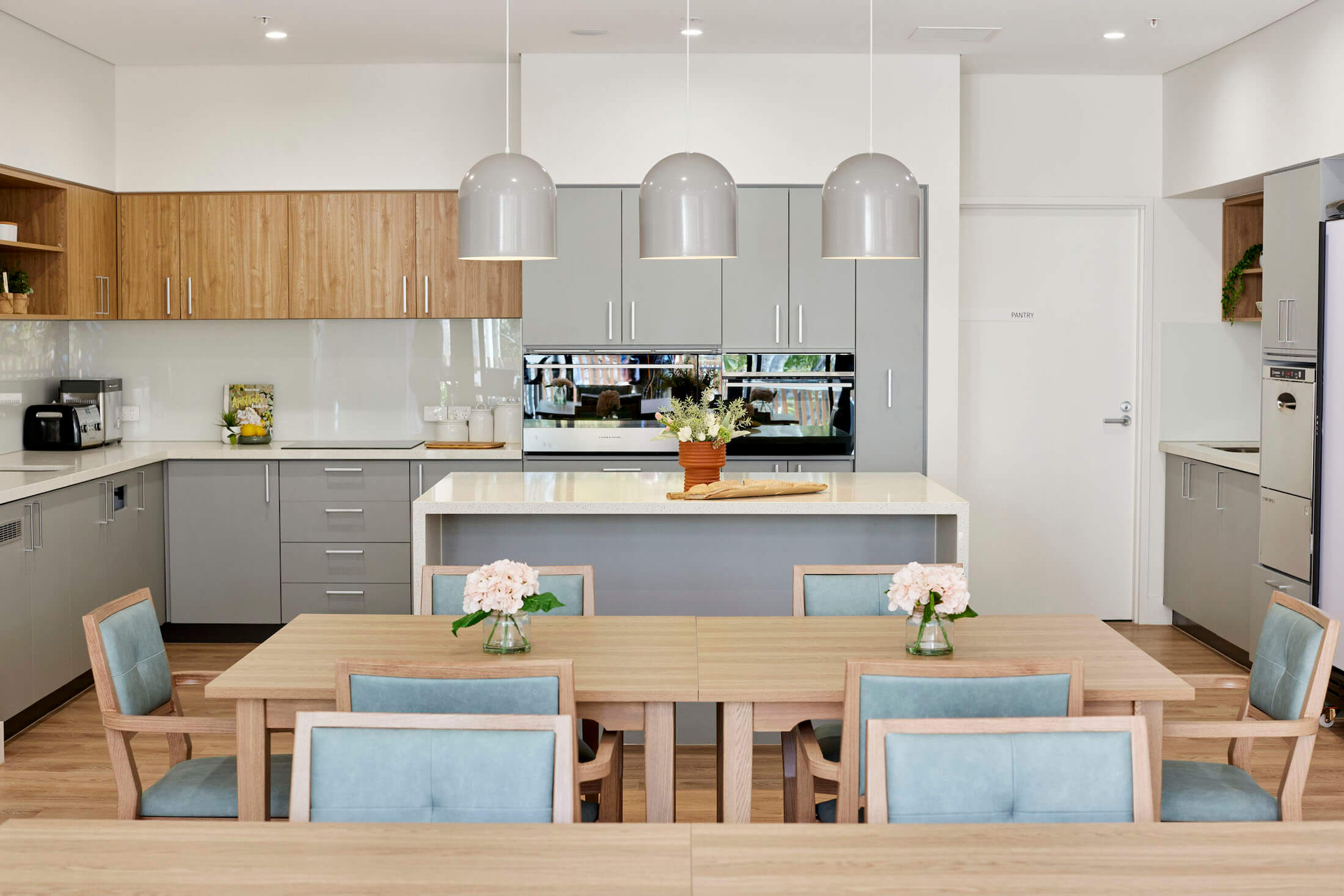 A new kitchen with grey pendant lights over an island bench, timber dining table in foreground