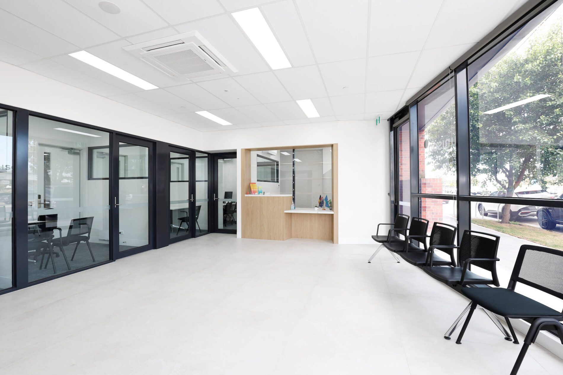 Bright building foyer with meeting rooms and concierge desk, black seating by window