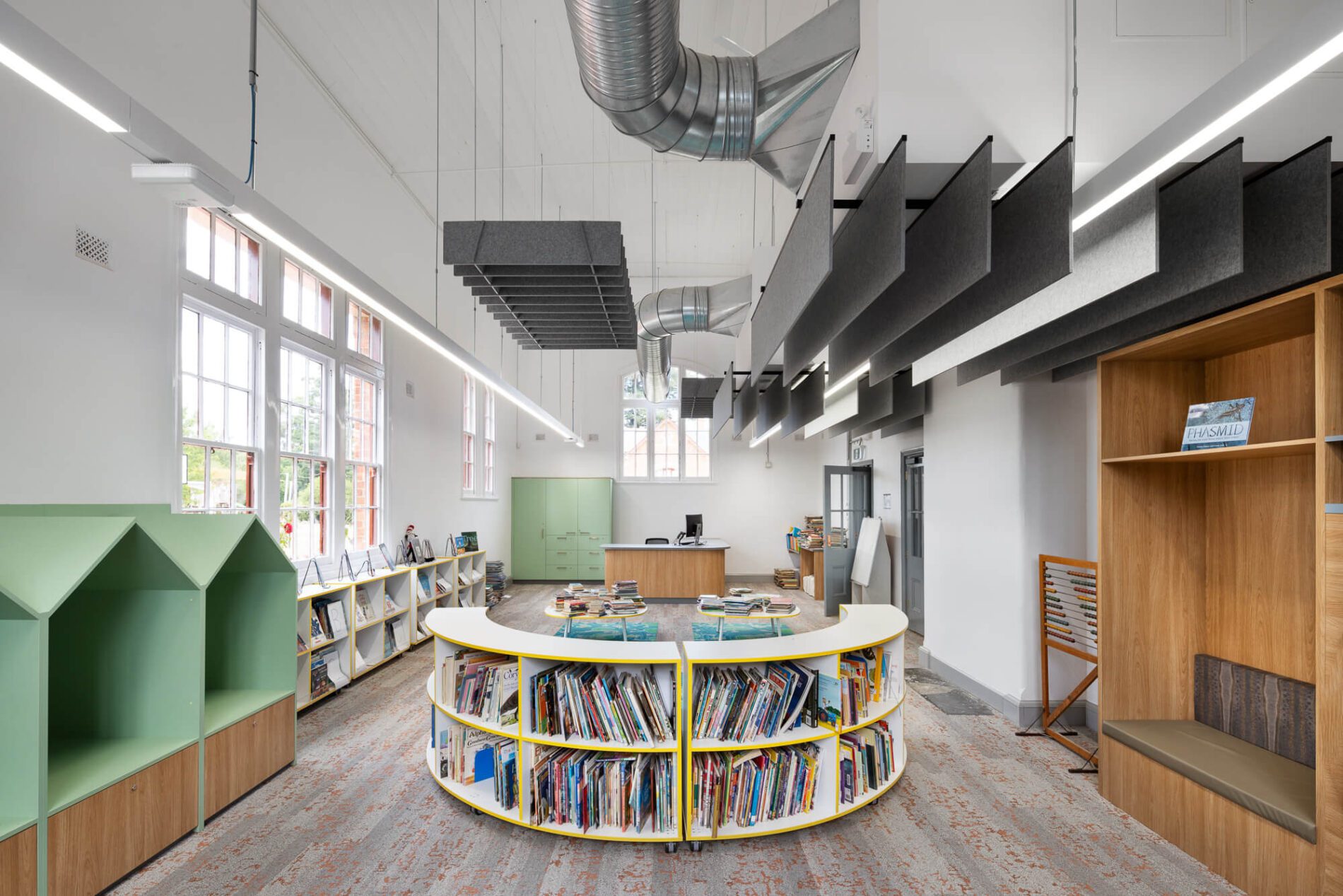Library space with acoustic ceiling baffles, book display and green, house-shaped cubby nooks