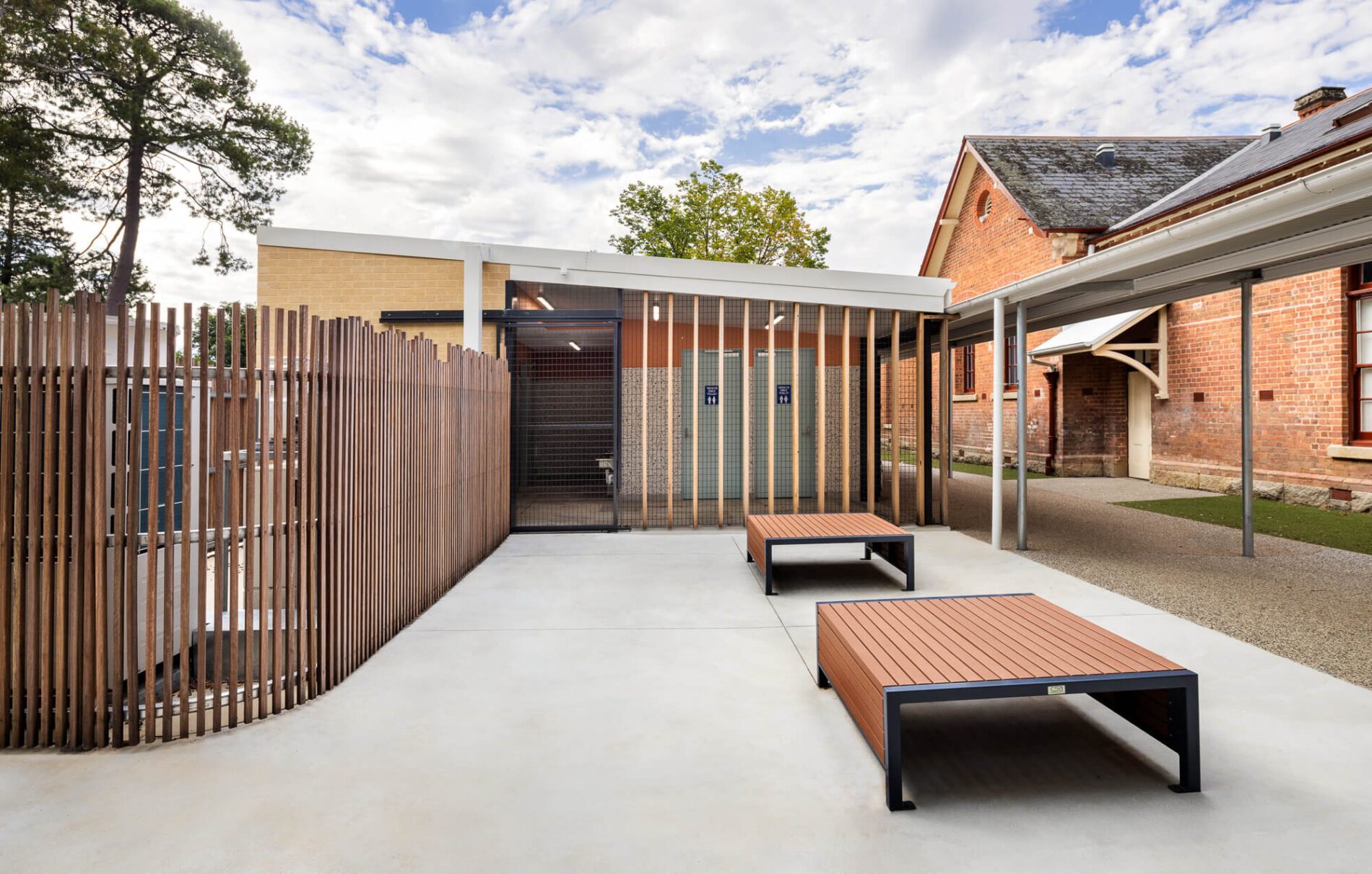 Outdoor paved seating area next to walkway, timber and metal screen to adjacent toilets