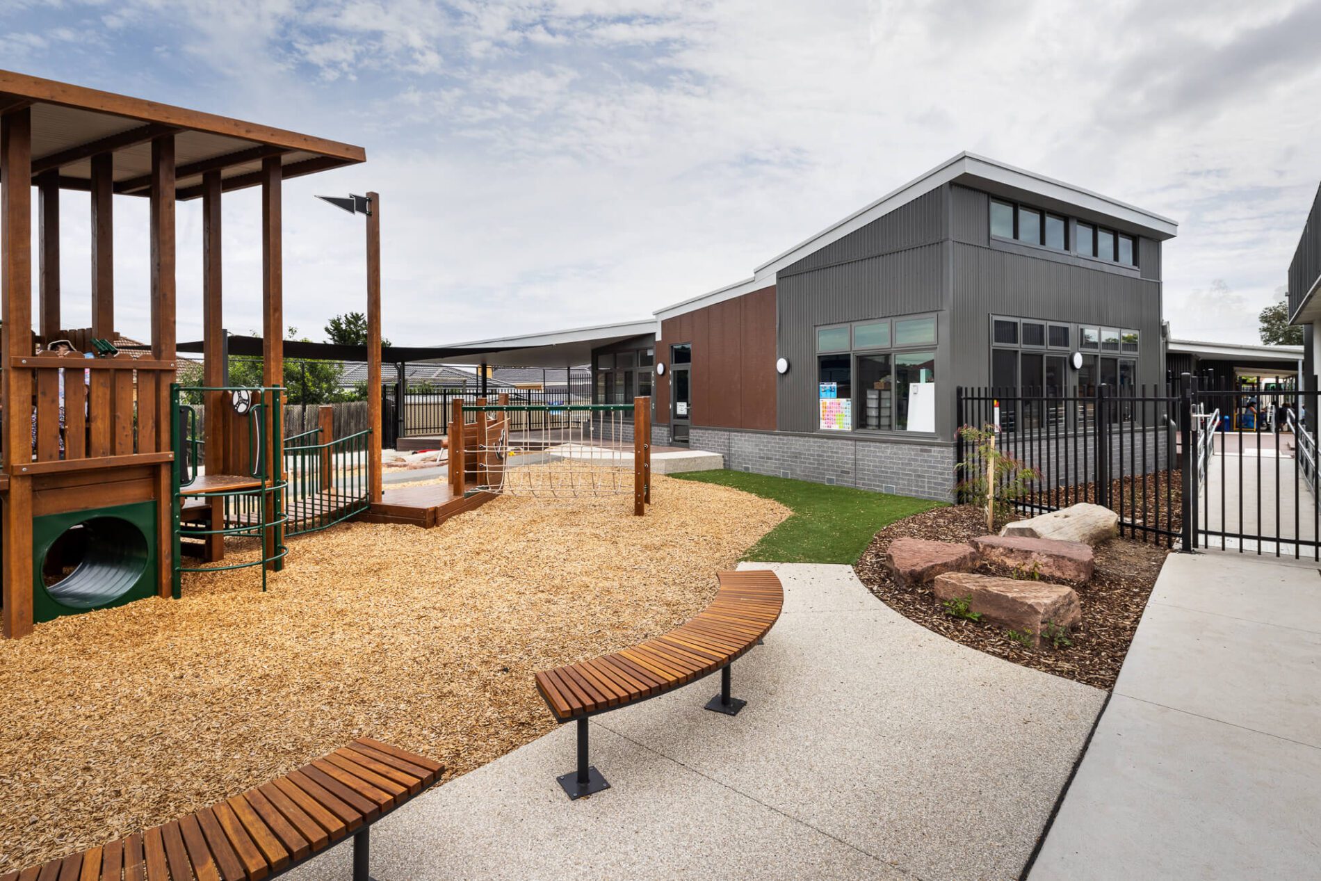 Outdoor play gym on soft fall bark, curved timber seating and classroom in background