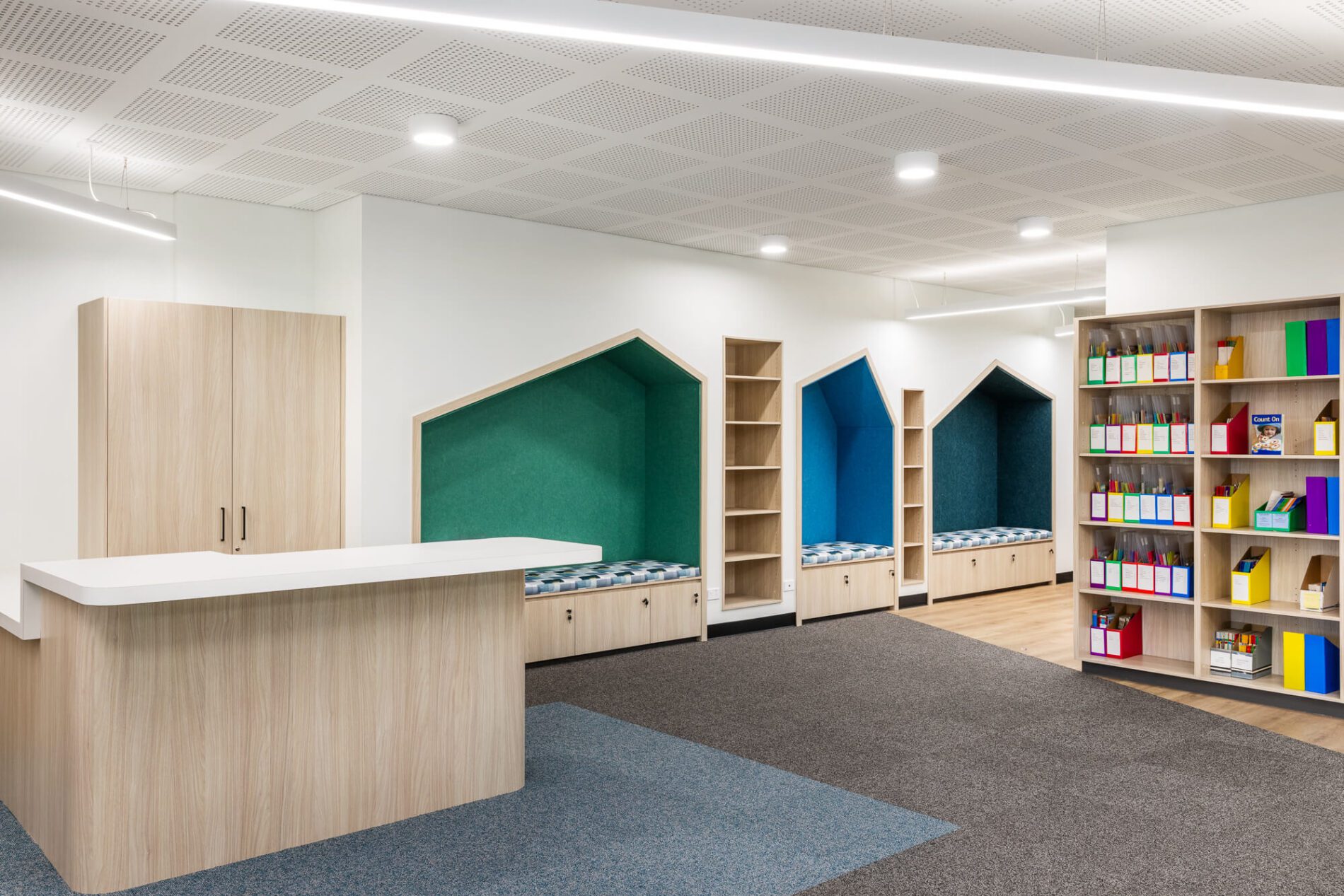 Coloured cubby reading and regulation nooks in playful asymetric house shapes, storage shelving and teacher's desk