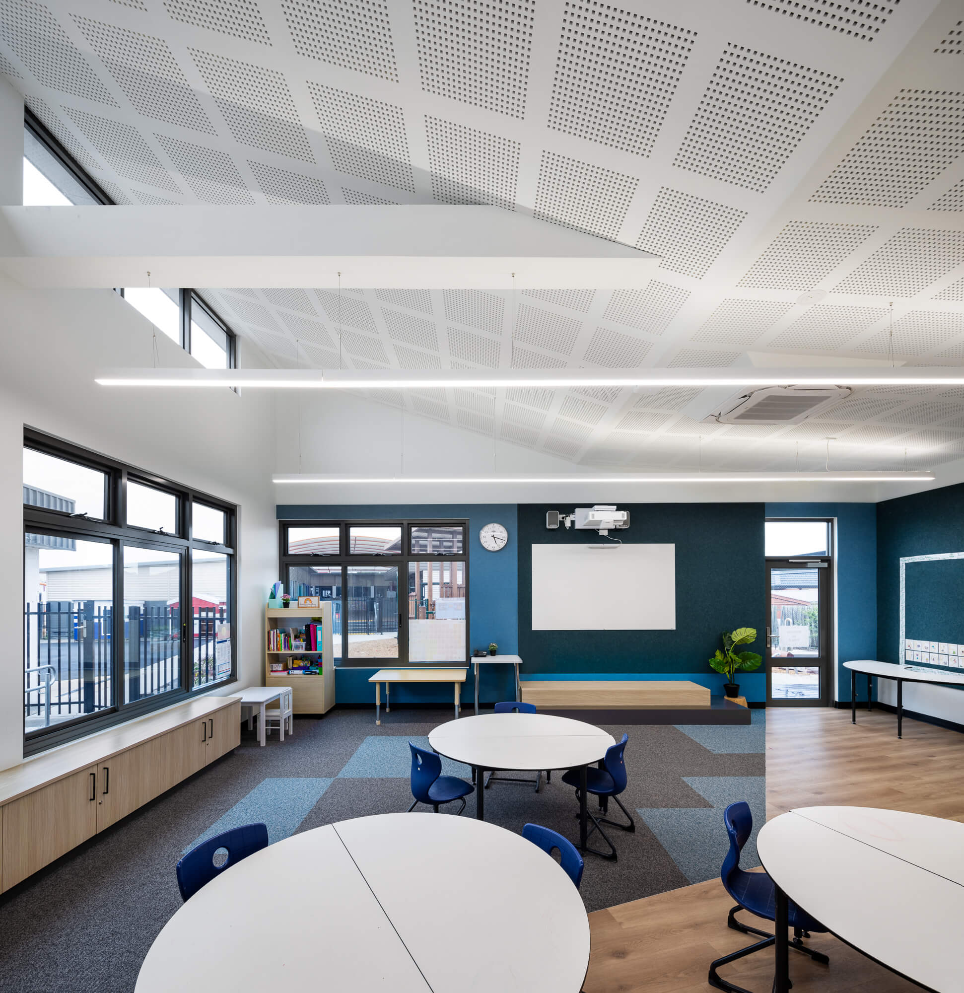 School room with round tables, student-heigh windows and raked white ceiling with perforated acoustic treatment.